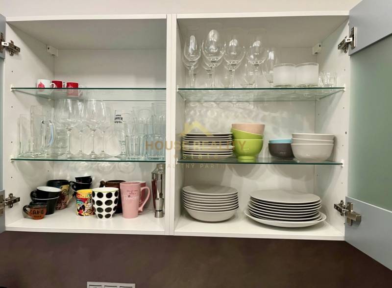 An open kitchen cabinet with glasses, cups, and plates in a 2-room apartment.