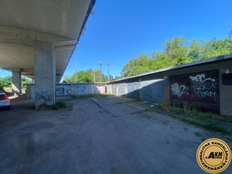 Garages in Zvolen under the bridge with graffiti on the walls and a parked car.