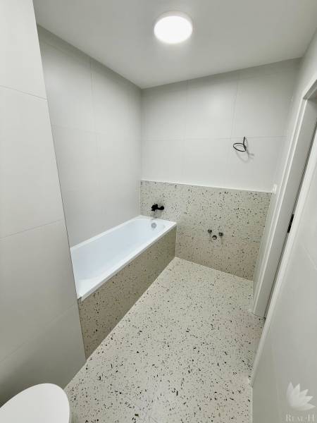 Bathroom in a 2-room apartment with a bathtub and light ceramic tiles.