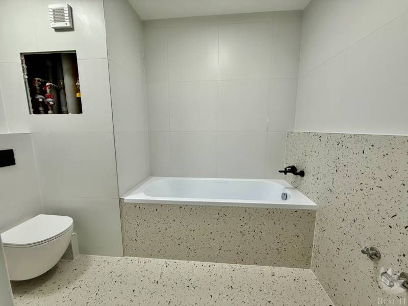 Bathroom with a bathtub and toilet in a 2-room apartment with white tiles.