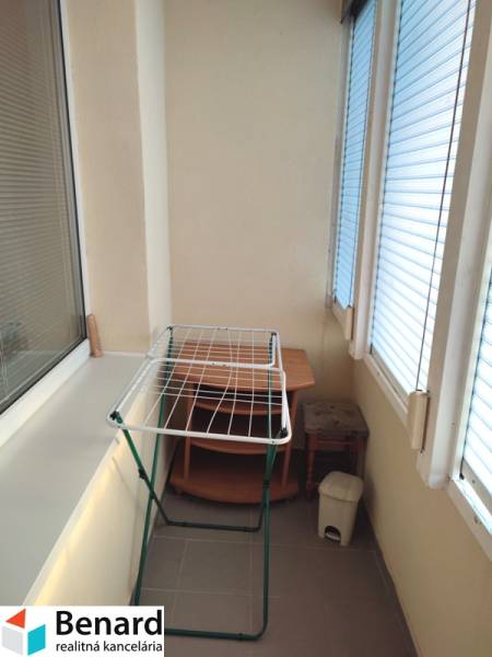 Glazed balcony in a 2-room apartment with a shelf, clothes dryer, and trash bin.