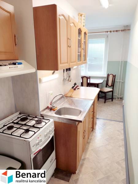 A kitchen in a 2-room apartment with a gas stove, sink, and wooden cabinets.