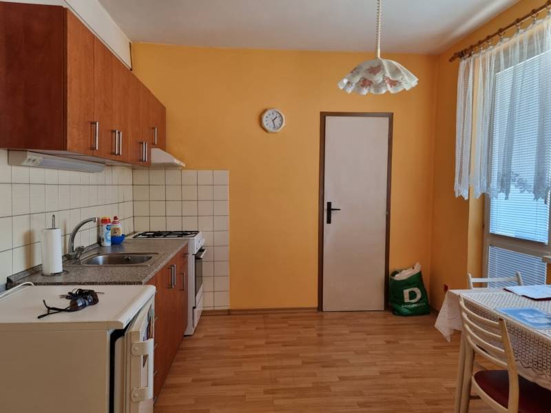 A kitchen in a 2-room apartment with orange walls, wooden floor, and a dining table.