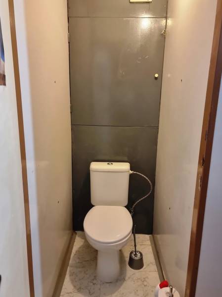 A toilet in a 2-room apartment with white marble floor tiles.