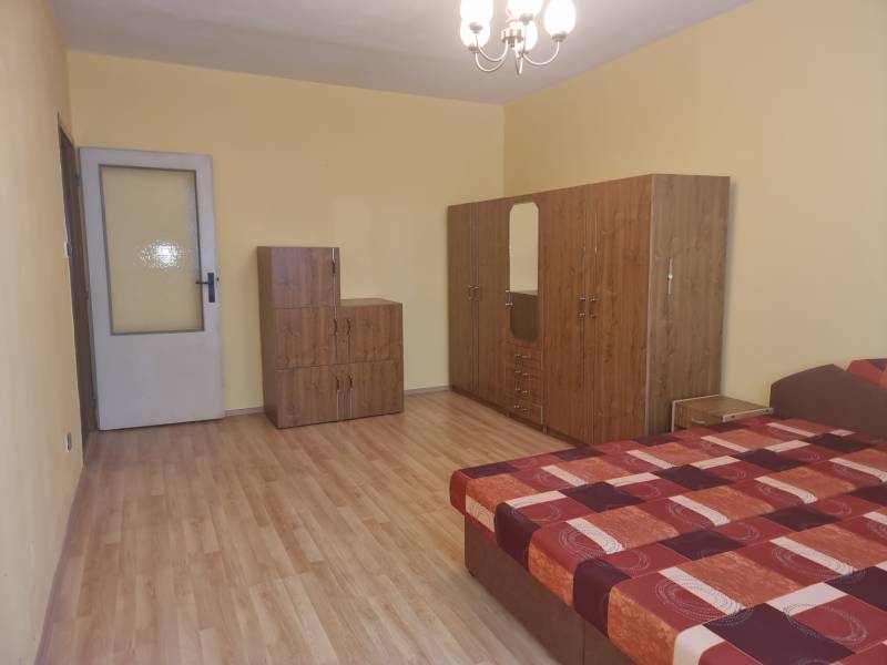 A room in a 2-room apartment with a bed, wardrobe, and dresser on a wooden floor.