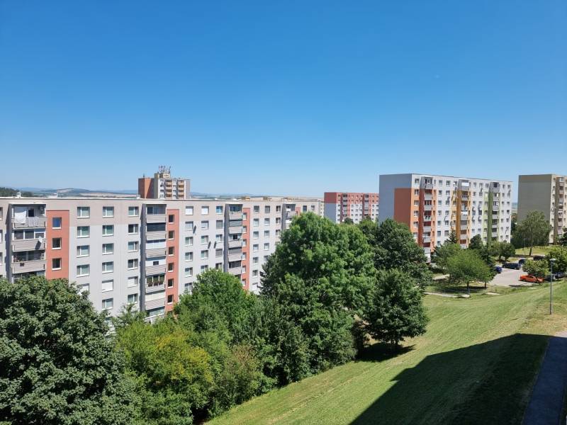 The housing estate with panel buildings on Petzwalova Street in Nitra, surrounded by greenery and a blue sky.
