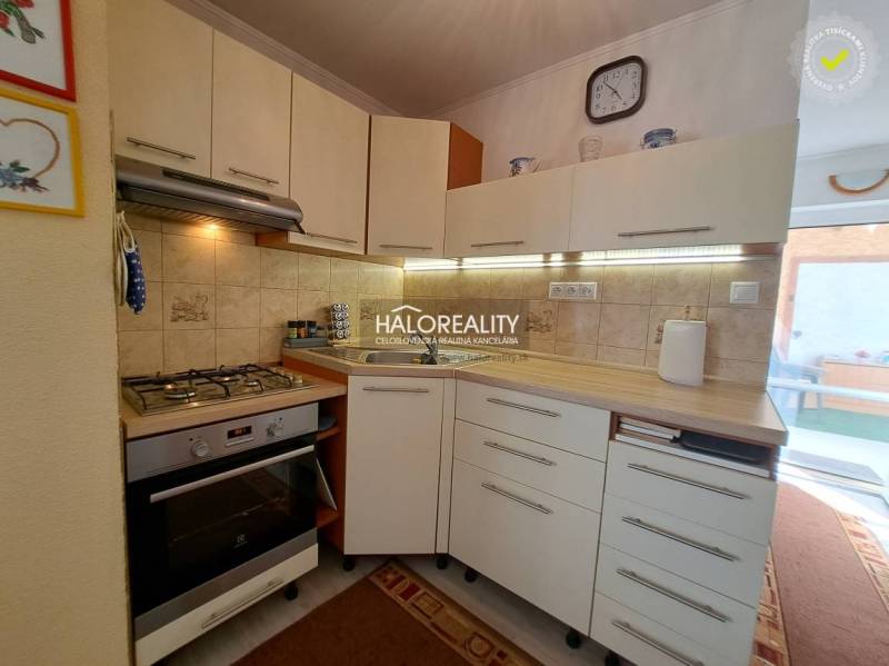 A kitchen in a family house with appliances, a sink, cabinets, a clock, and decor on the tiles.
