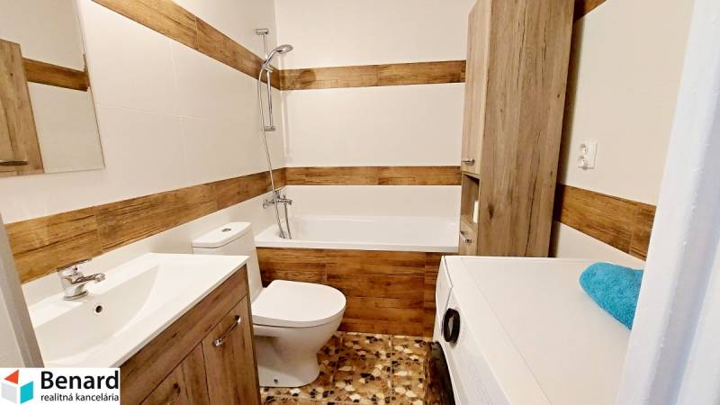 Bathroom in a studio apartment with a bathtub, washing machine, toilet, and wooden details.