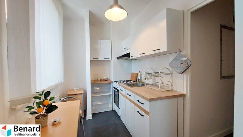 A kitchen in a studio apartment with a wooden counter, white cabinets, and a dining table.