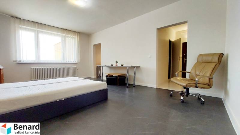 A bedroom in a studio apartment with a bed, a desk, and a chair.