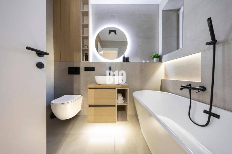 A modern bathroom with a bathtub, mirror, and toilet in a 3-room apartment on Benediktiho Street.