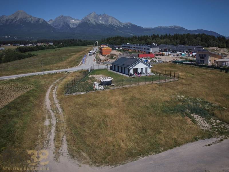 Residential plots in Mlynica with a view of the Tatras, a country house, and buildings in the background.