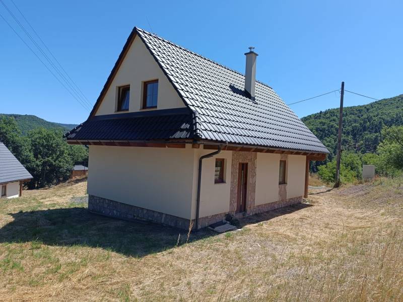 A cottage in Horné Hámre with a metal roof and surrounding nature, under a blue sky.