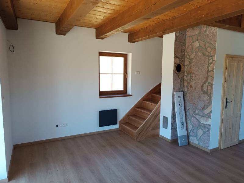 Interior of a cabin with a wooden ceiling, stairs, and a stone wall.