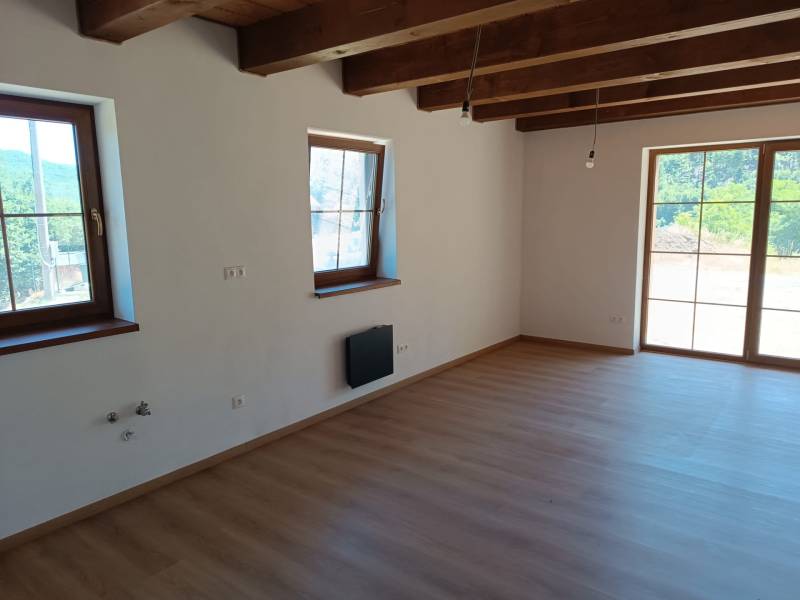 The interior of the cottage with light walls, wooden beams, and large windows for natural light.