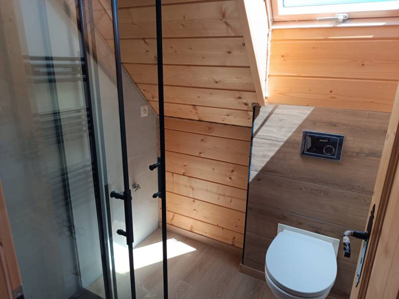 A bathroom in a cabin with a shower and wooden paneling under a skylight.