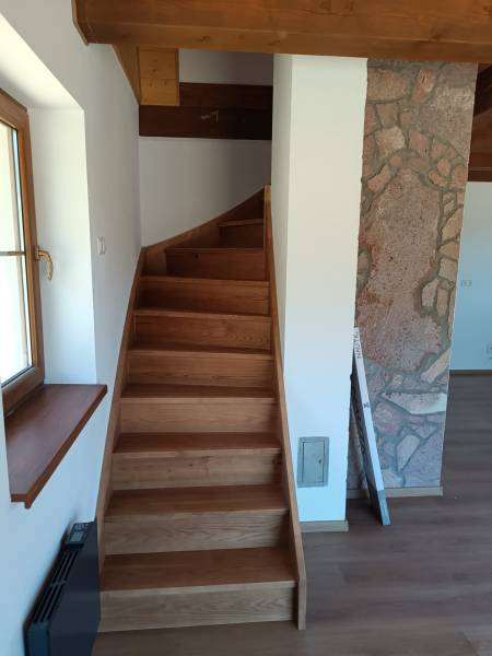 Wooden stairs in a cabin with a stone wall and a window.