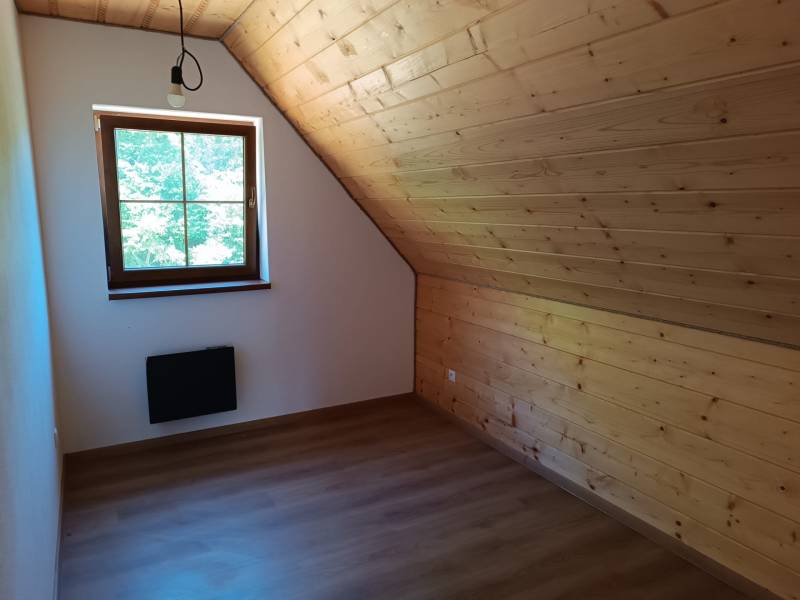 Attic room with wooden paneling, a window, and simple lighting in a cabin.
