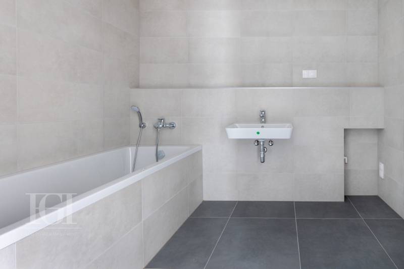 A bathroom with a bathtub and a sink in a 3-room apartment with neutral tiles.