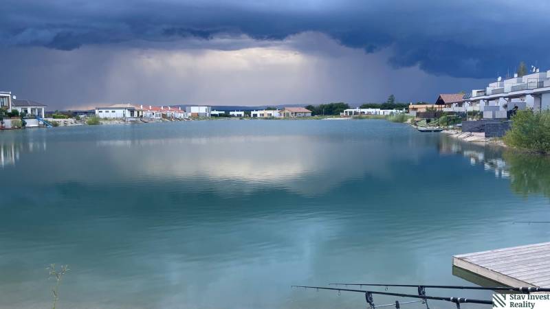 A lake surrounded by houses in Boldog, residential plots, dramatic sky before a storm.