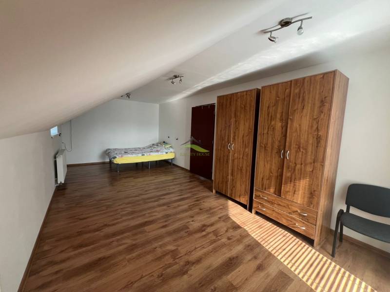 Attic room in a family house with a bed, wardrobes, and wooden floor.