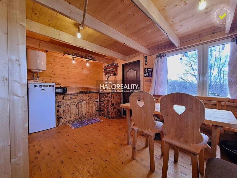 Interior of a cabin with wooden furniture and a kitchen area, with a view of the surroundings.