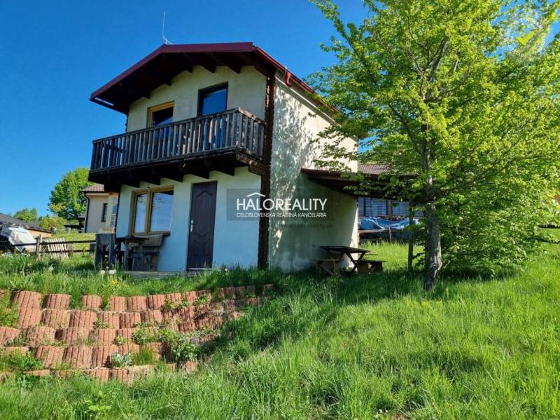 A cottage in Počúvadlo with a wooden balcony and greenery on the slope.