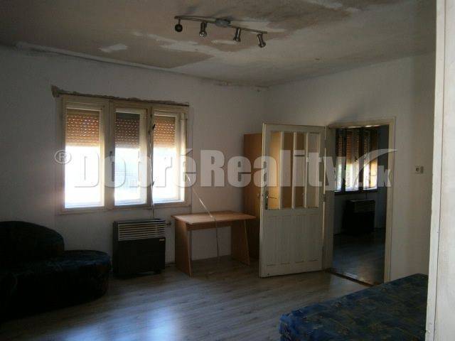 A bright room in a family house includes windows, a sofa, a table, and open doors.