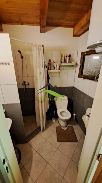 A bathroom in a cabin with tiles, a shower, a toilet, and a wooden ceiling.