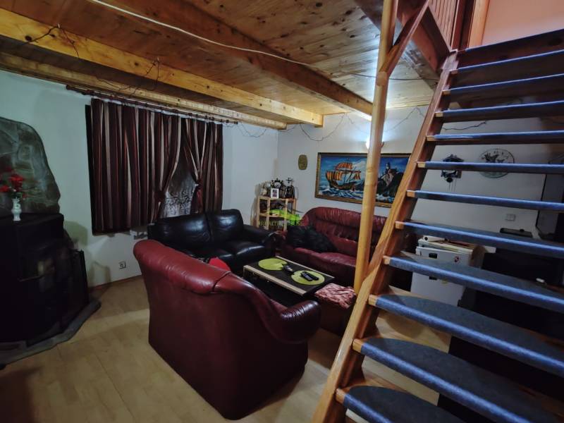 The interior of a cabin with a wooden ceiling, sofas, and a staircase leading to the upper floor.