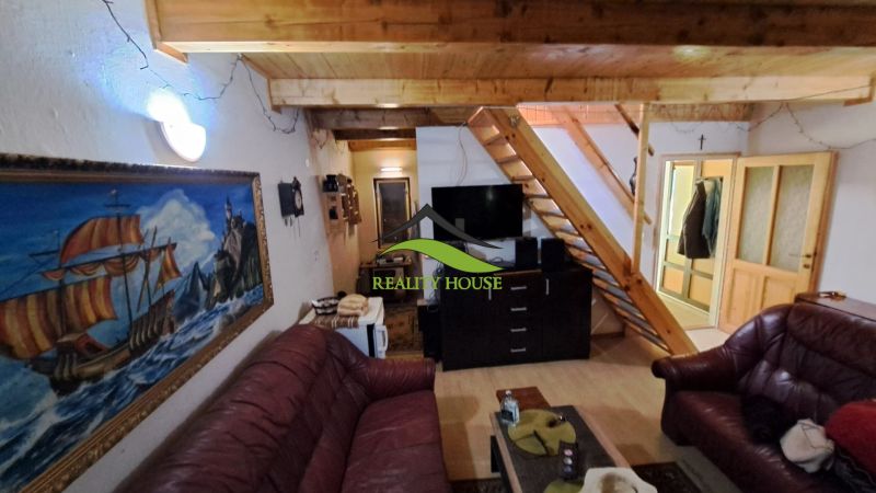 Living space in a cabin with a staircase, leather sofas, and a wood-patterned floor.