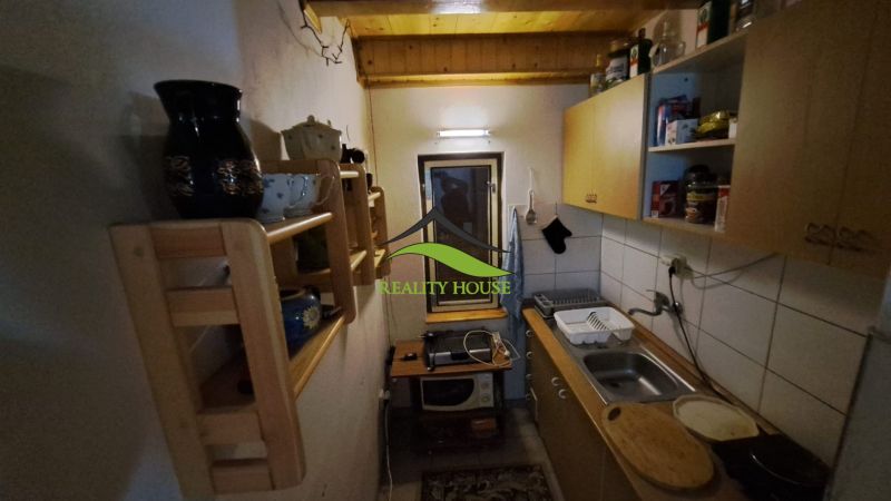 A narrow kitchen in a cabin with a wooden ceiling, shelves, and basic equipment.