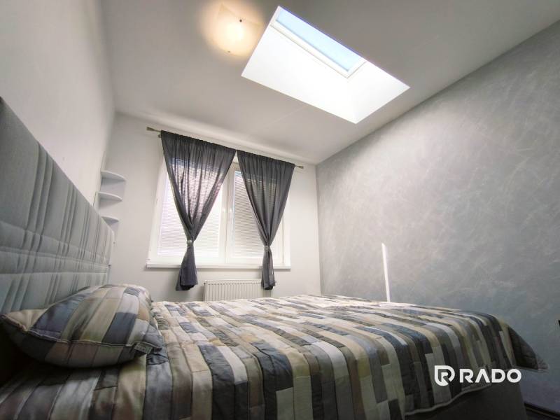 Bright bedroom in a 2-room apartment with a bed, large window, and skylight.