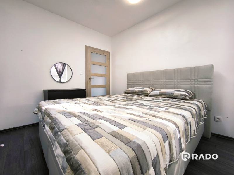 Bedroom in a 2-room apartment with a large bed and a mirror on white walls.