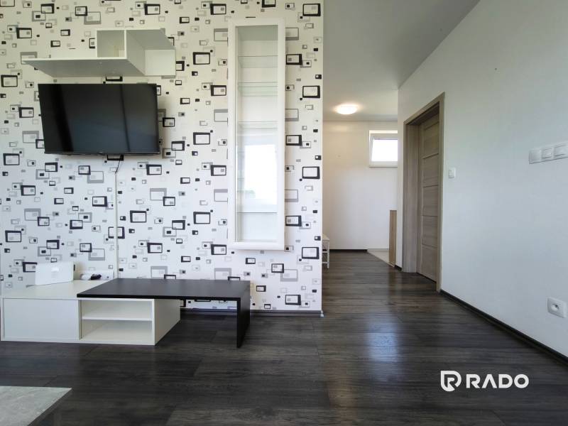 Interior of a 2-room apartment with a television on a patterned wall and dark flooring.