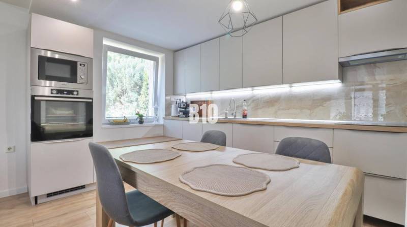 A kitchen in a family house with a dining table, built-in appliances, and a large window.