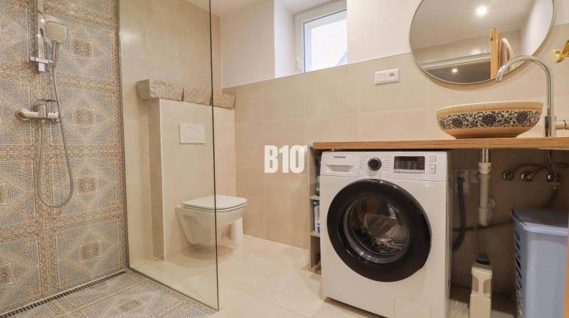 A bathroom in a family house with a washing machine, shower cabin, and decorative sink.