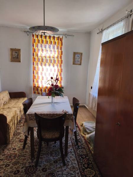 Dining room in a family house with a table, chairs, flowers, carpet, and curtain.