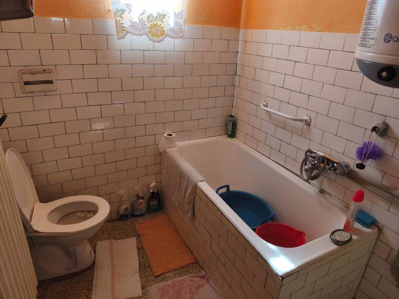 Bathroom in a family house with white tiles, a bathtub, and a toilet.