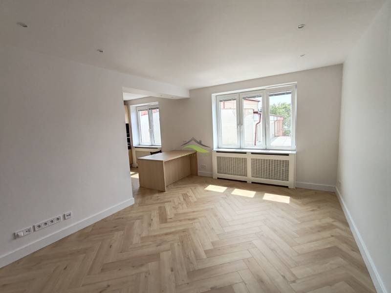 Bright living room in a two-room apartment with wooden flooring and windows.