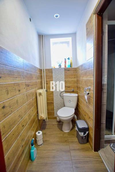 A bathroom with wooden paneling in a family house, window, radiator, and basic equipment.