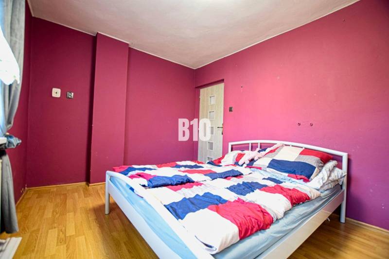 A bedroom with a light-colored bed, colorful walls, and parquet flooring in a family house.