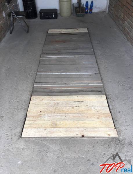 A wooden platform on the garage floor. Various items and storage space in the background.