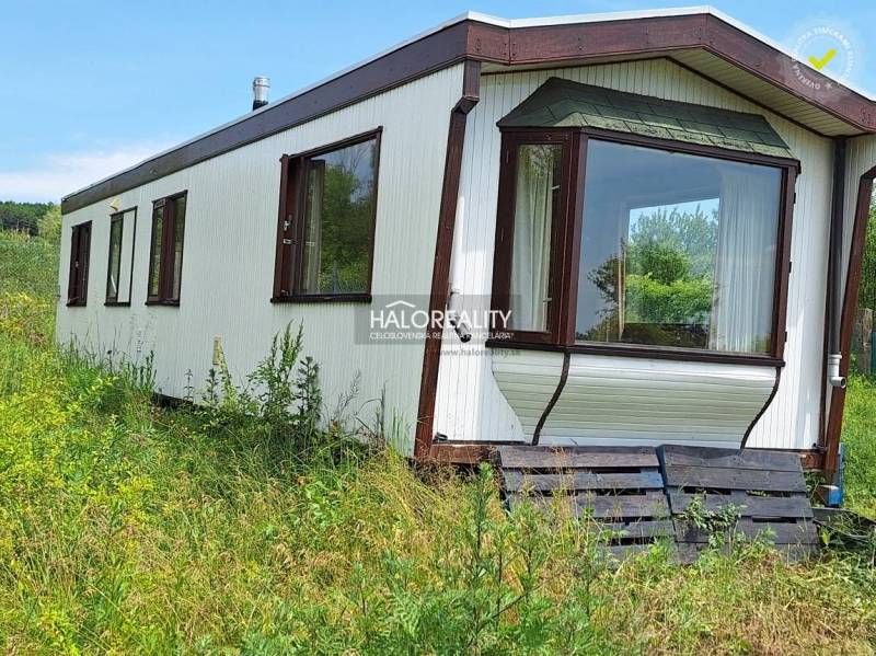Boleráz: A cabin surrounded by nature with a glass veranda, grassy surroundings, and pallet stairs.