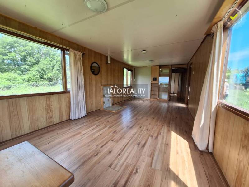 Interior of a wooden cabin with large windows and light flooring.