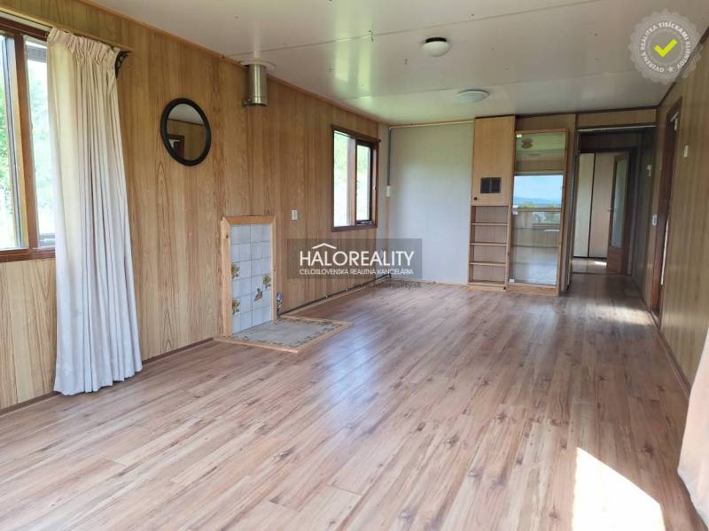 Interior of a cabin with wooden paneling and laminate flooring, light walls and windows.