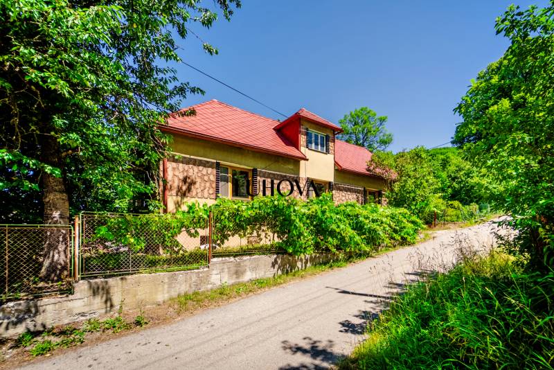 A family house on a quiet street in Púchov with lush greenery and a fence.