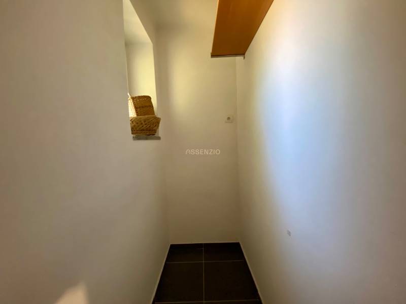 A narrow hallway with a bright sign in a 2-room apartment, a basket, and shelves on the wall.