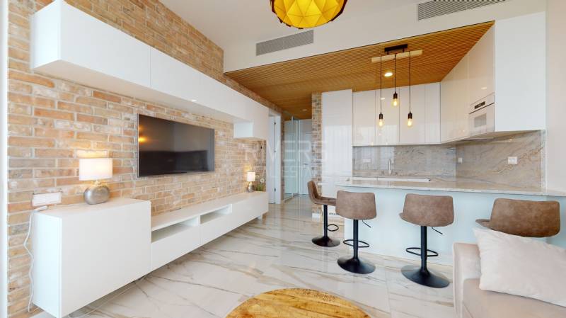Living room in a 2-room apartment with a brick wall, kitchen island, and bar stools.