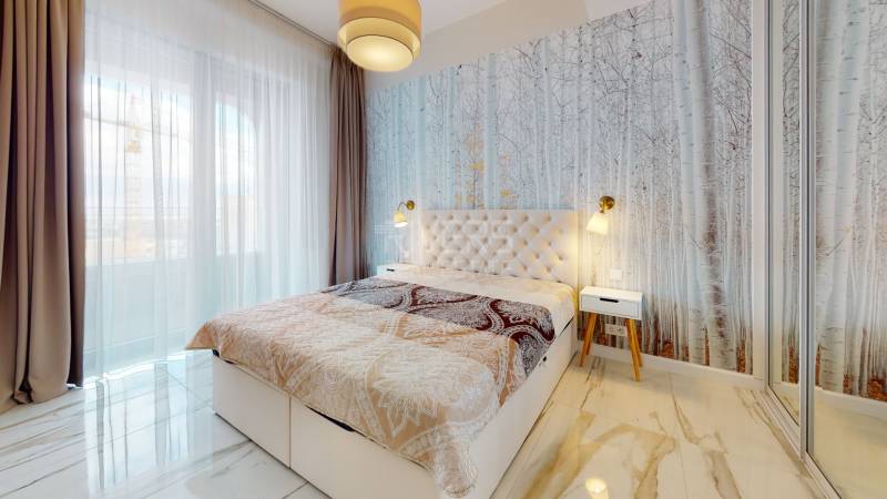 A bedroom with a nature motif on the wallpaper, a large window, and a mirrored wardrobe in a 2-room apartment.